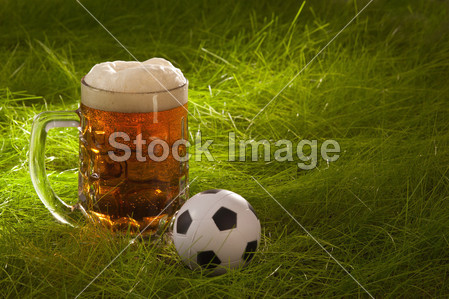 马克杯的鲜啤酒和小足球在草地上图片素材(图