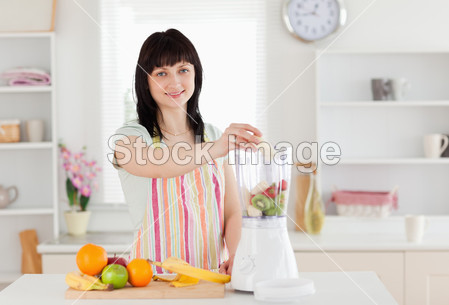 可爱深色头发的女人,把蔬菜放在站立时混音器