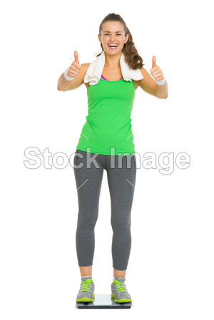 快乐健身年轻女人站在体重秤上,显示的拇指图